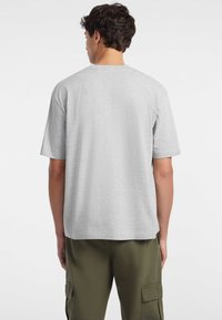 Camiseta de algodón gris con mangas cortas, escote redondo y corte relajado, vista desde la parte posterior contra un fondo sencillo.