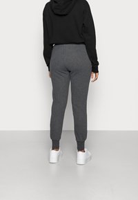 Graue Jogginghosen aus weichem Stoff, an den Knöcheln schmal zulaufend, kombiniert mit einem schwarzen Hoodie und weißen Turnschuhen. Einfaches, lässiges Design.