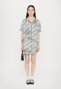 Camicia a maniche corte con colletto e gonna abbinata in un motivo astratto bianco e nero, con una finitura texturizzata e rifiniture nere. Tiene una piccola borsa nera.
