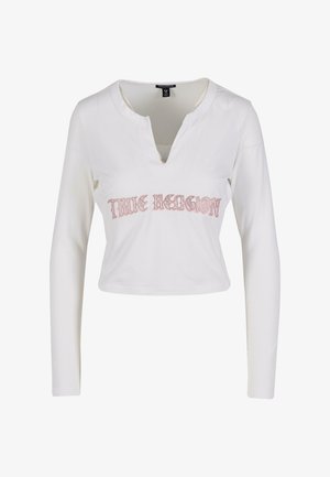 Bela dolga majica s kratkimi rokavi, ki ima V-izrez in rožnato vezeno besedilo "TRUE RELIGION" čez prsi. Mehka bombažna tkanina.