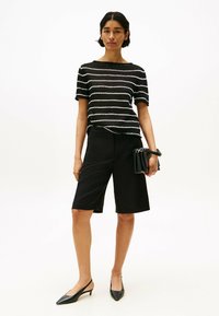 Maglietta a righe bianco e nero a maglia, maniche corte, abbinata a pantaloni bermuda neri su misura. La modella tiene una piccola borsa nera. Scarpe slingback nere.