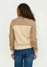 Bež i smeđi pleteni kardigan s uzorkom ovratnika, rebrastim manžetama i rubom, te kontrastnim blokom boje na leđima. Teksturna i mekana tkanina.