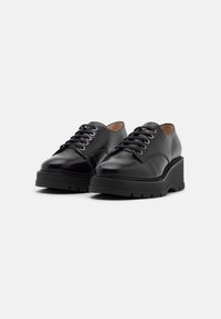 Scarpe in pelle nera con punta rotonda e suola piatta spessa, caratterizzate da un design tradizionale con lacci e occhielli metallici a contrasto.