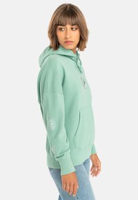 Mint green hoodie made of soft material, featuring a front pocket, sun graphic on the sleeve, and drawstring hood.