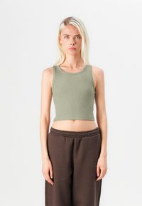 Rebrasti, bezrukavni crop top u prigušenoj zelenoj boji. Mekani, rastezljivi materijal s okruglim izrezom. Uparen s širokim, tamnosmešim trenerkama.