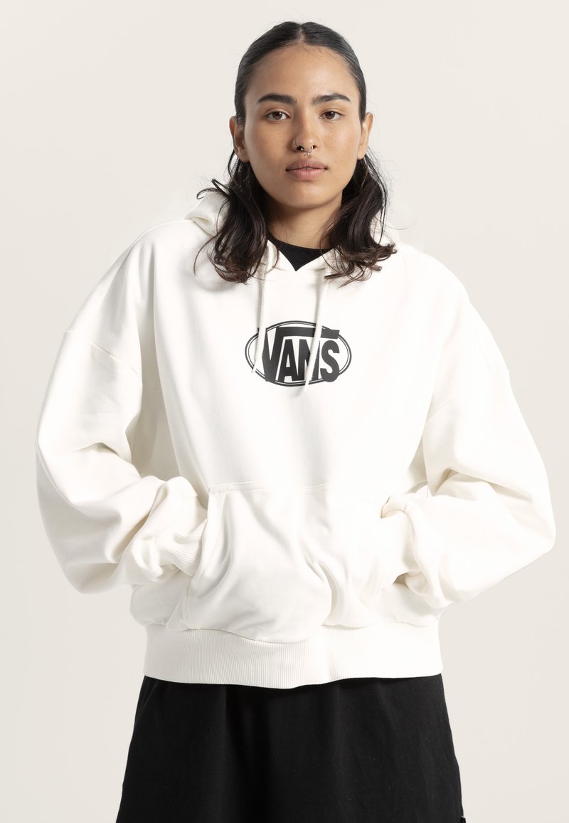 Sweat-shirt à capuche blanc avec un logo Vans noir, poche avant et poignets côtelés. Porté sur un t-shirt noir, présenté sur un fond neutre.