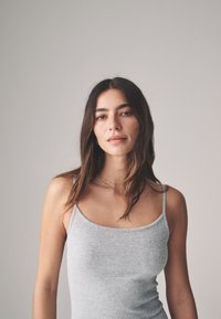 Šedé rebrované tielko s tenkými ramienkami, priliehavý strih, jemná textúra a výstrih do lodi. Jednoduché pozadie pre kontrast.