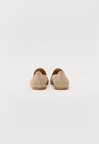 Beige semskede slip-on sko med lav profil og buet bak, med en jevn tekstur og minimalt detaljer.