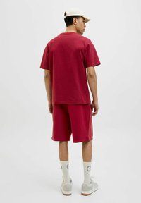 T-shirt en coton rouge à manches courtes assortie à un short rouge. Chaussettes blanches et baskets gris clair. Fond neutre.