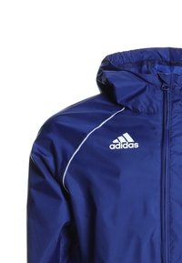 Granatowa sportowa kurtka z zamkiem z przodu, elastycznymi mankietami i kapturem. Posiada białe akcentujące linie oraz logo Adidas na piersi.