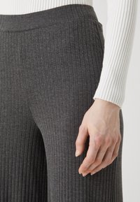 Gray ribbed wide-leg pants with a high waistband. The fabric appears soft, stretchy, and textured, complementing a fitted white ribbed top.