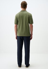 Polo verde oliva a maniche corte, abbinato a pantaloni blu scuro. L'outfit presenta un design semplice e pulito, con una texture di tessuto morbido.