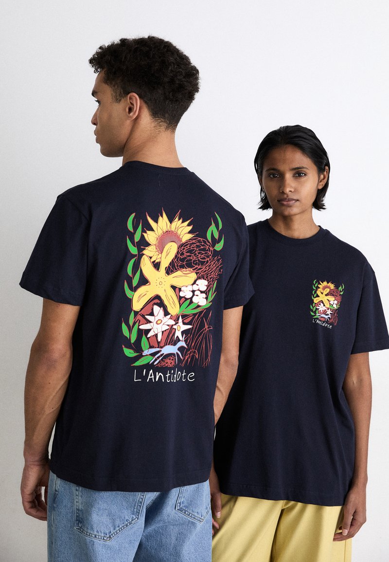 Marineblå bomulds T-shirts med farverige blomstertryk på ryggen og et mindre design på fronten. Løs pasform, korte ærmer.