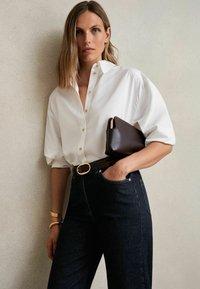 Vit skjorta med uppvikt ärmar, mörka jeans i hög midja och en mörk kuvertväska. Utrustad med ett bälte med guldfäste och ett metallarmband.