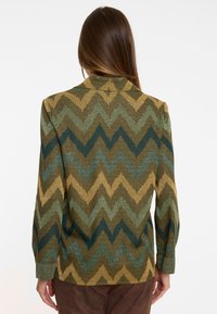 Texturierter Blazer mit einem Zickzackmuster in Grün-, Gold- und Brauntönen; verfügt über einen klassischen Kragen und lange Ärmel.