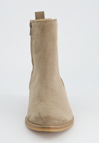 Beezsuede pahklitossudest, millel on ümmargune nina, külgkrõpsuga lukk ja madal kummitald. Tagaküljel on käepide.