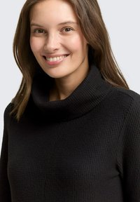 Pull noir à col cheminée en tissu texturé, coupe ajustée avec accents côtelés. Comprend un col dégagé et des manches longues.