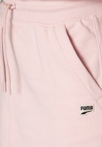 Pantalons de survêtement en coton rose avec une taille à cordon de serrage réglable, poches latérales et un petit logo Puma noir en bas à droite.