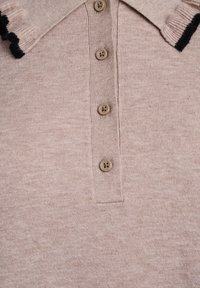 Maglietta polo beige con una texture a coste, dotata di un colletto con rifiniture nere e cinque bottoni rotondi marroni sul davanti.