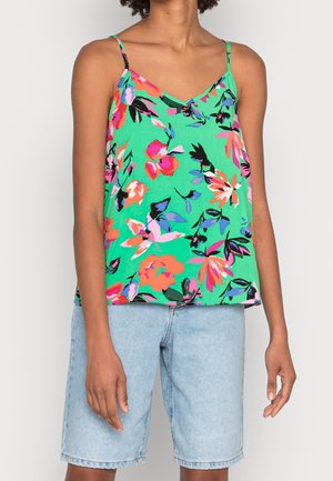 Person iført grøn floral spaghetti-strop top med pink, orange og blå blomster kombineret med lyseblå denimshorts.