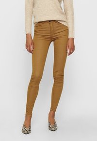 Jeans ajustados color beige con una textura suave, diseño clásico de cinco bolsillos y un ajuste de altura media. Combinados con planos puntiagudos de patrón.