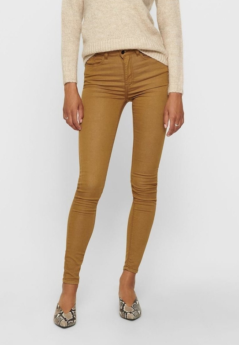 Jeans ajustados color beige con una textura suave, diseño clásico de cinco bolsillos y un ajuste de altura media. Combinados con planos puntiagudos de patrón.