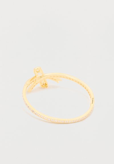 Aranyszínű fémből készült karkötő, sima felülettel és egyik oldalán egy sor tiszta strasszkővel. Csuklós kapocs a biztos viseletért.