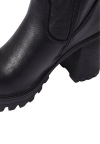 Stivaletto in pelle nera con finitura testurizzata, cerniera laterale e tacco chunky con battistrada per una maggiore aderenza. Presenta cuciture e rifiniture lisce.