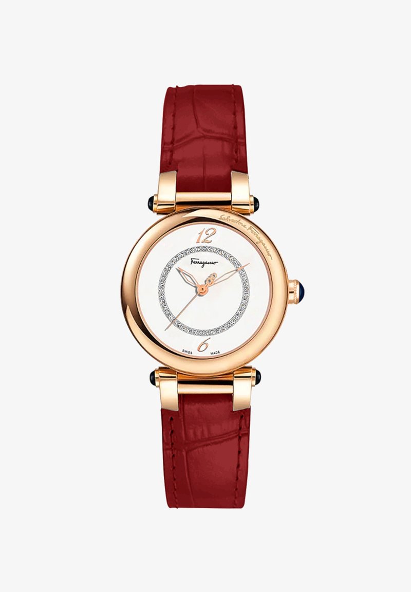 Roosa kuldne kell valge näo, punase krokodilliküreeritud nahkraami, teemandiga aktsentside ringi ja sinise kalliskiviga kroonil.