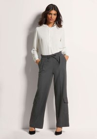 Weißes Hemd mit Knopfleiste und Kapuze, kombiniert mit grauen, hochtaillierten, weit geschnittenen Hosen mit Taschen und einem Kordelzugbund.