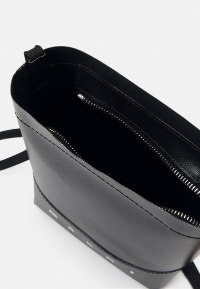 Sac en synthétique noir avec fermeture éclair, texture lisse et couture visible. L'intérieur est uni ; logo à l'avant. Sangle réglable incluse.
