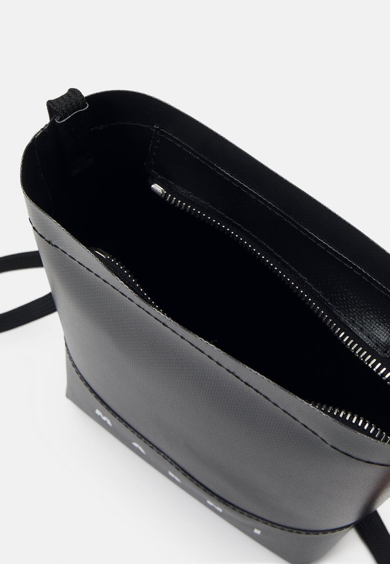 Borsa nera in materiale sintetico con chiusura a zip, texture liscia e cuciture visibili. L'interno è privo di motivo; logo sulla parte anteriore. Strappo regolabile incluso.