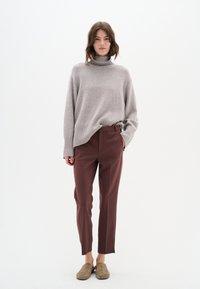 Gai pelēks adīts turtlenecks džemperis ar ribotu apakšmalu, apvienots ar pieguļošām tumšbrūnām biksēm un taupe slip-on apaviem. Vienkāršs dizains, gluda auduma tekstūra.