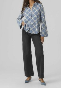 Blå mönstrad skjorta med vitt diamantmönster, knäppning framtill, vida ärmar; matchas med mörka denimjeans och ljusblå klackar.