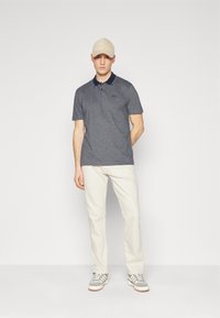 Vīriešu polo krekls tumši pelēkā krāsā ar jūras zilas krāsas apkakli un baltām detaļām, saskaņots ar krēmkrāsas biksēm un pelēkiem sporta apaviem. Beisbola cepure gaiši bēšā krāsā.