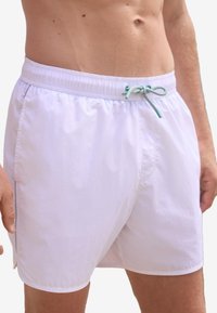 Hvide badeshorts med elastisk talje og turkis snøre. Har sidelommer og en glat, let tekstur.