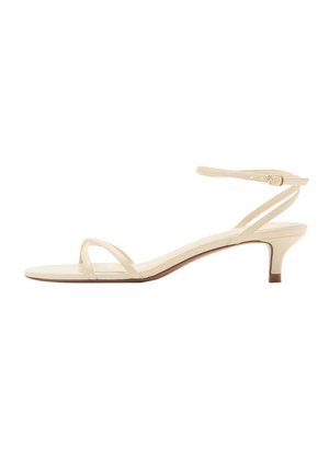 Sandale beige à talon bas avec fines brides, bout ouvert et bride à boucle à la cheville sur fond blanc.