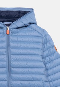 Ανοιχτό μπλε μπουφάν με κουκούλα και ραφή καπιτονέ, με εμπρός φερμουάρ και πορτοκαλί τράβηγμα φερμουάρ, εμφανίζεται από το στήθος και πάνω σε λευκό φόντο.