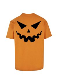 Oransje bomull t-skjorte med et stort svart jack-o'-lantern grafikk på baksiden, med trekantede øyne og et tagget munn-design.