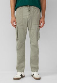 Lichtgroene cargo shorts met een trekkoord in de taille, meerdere zijzakken en gestikte details. Draagt met witte sneakers.