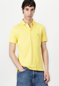 Gelbes Poloshirt aus Baumwolle, mit klassischem Kragen, Knopfleiste und kleinem Logo auf der Brust, kombiniert mit blauen Jeans.