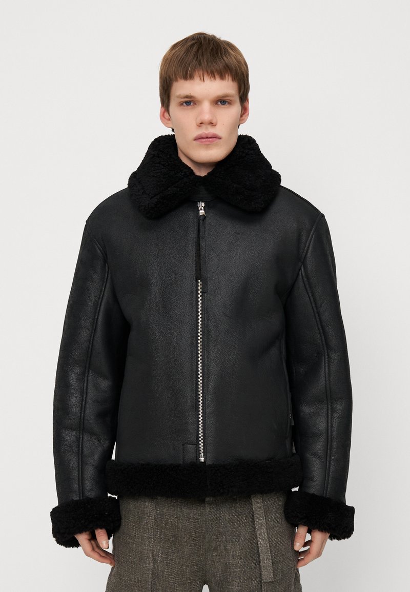 Chaqueta de cuero negra con un collar y puños de pelo negro texturizado, con una cremallera frontal y un corte relajado.