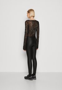 Fekete áttetsző, hosszú ujjú blúz hímzett virágmintákkal, hozzá illő, fényes anyagú fekete leggings, sötét sportcipőkkel párosítva.