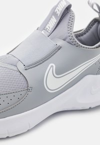 Vaaleanharmaat Nike-liukosneekkerit, joissa on valkoinen swoosh-logo, joustava nauha ylhäällä, verkkokankainen kärki ja valkoinen kumipohja.