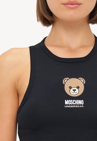 Melna bezviedera blūze, izgatavota no gludas auduma, ar lāča grafiku un baltu uzrakstu "Moschino Underbear" zem attēla.