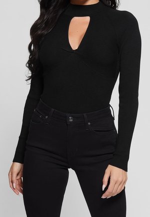 Schwarzer, gerippter Langarm-Body mit einem Schlüsselaugen-Ausschnitt vorne, kombiniert mit hochgeschnittenen schwarzen Jeans. Glatte Textur, figurbetontes Design.