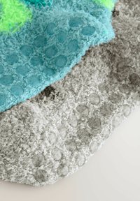 Texturerade filtar i teal och grått, med upphöjda prickmönster. Teal har livfulla gröna accenter, medan grått är mjukt och dämpat.