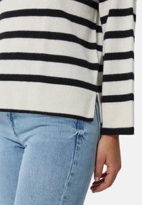 Maglione a righe bianche e nere realizzato in morbido tessuto a maglia, con orlo a coste e aperture laterali; abbinato a jeans in denim azzurro chiaro.