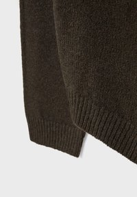 Gros plan sur la manche et l'ourlet d'un pull en tricot marron foncé avec des poignets côtelés, sur un fond uni clair.