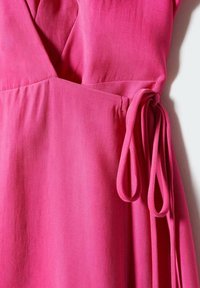 Robe portefeuille rose vif avec décolleté en V et détail de ceinture à la taille sur un fond clair uni.